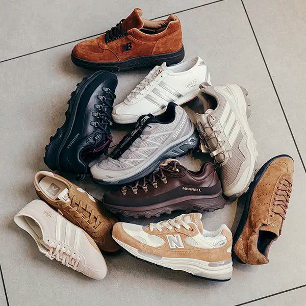 A circle of various autumn sneakers on a tiled floor. The shoes, in earthy tones like brown, beige, and white, include both athletic and casual styles.