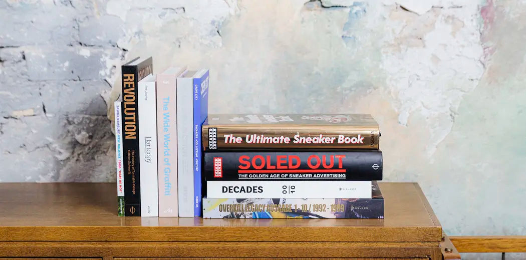 A stack of books on a wooden dresser, with magazines for men.