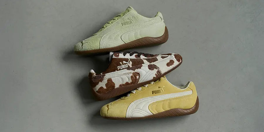 Three Puma Speedcat sneakers aligned diagonally on a gray surface, showcasing different designs: green, cowhide pattern, and yellow with a brown sole.