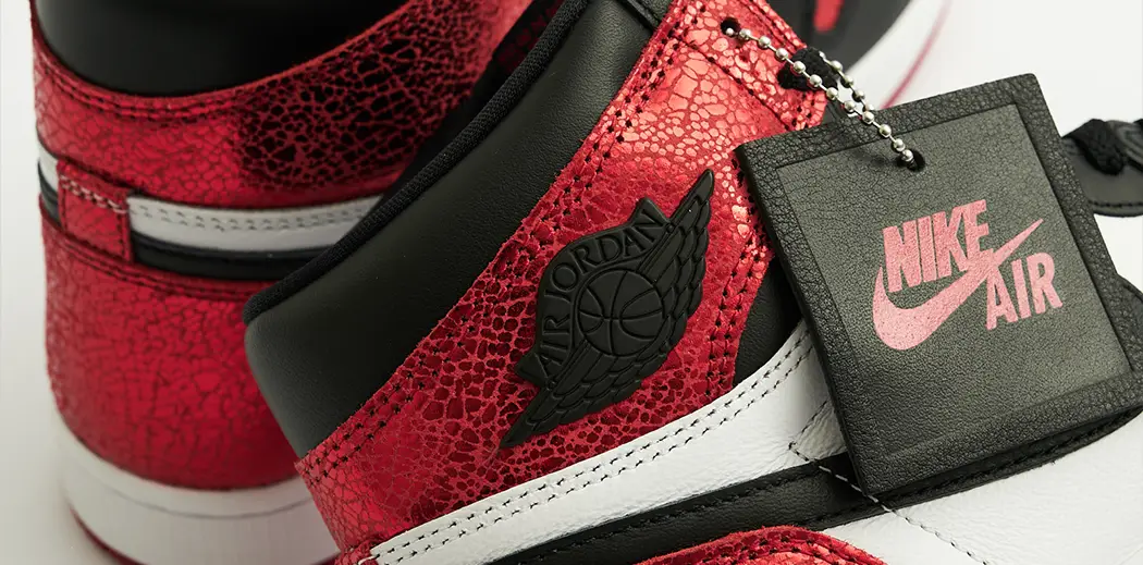 A pair of vibrant red and black Air Jordan 1 High Top sneakers with cracked texture and a visible Nike logo. The shoes have a stylish, modern design on a white background.