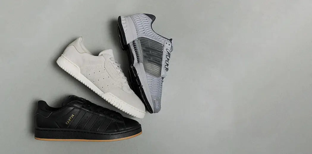 Three men low top sneakers are arranged diagonally against a gray background. From top: gray with mesh design, cream with suede texture, and black with branding.