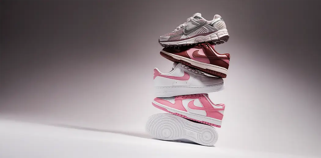 A stack of four stylish sneakers against a soft gray background: metallic gray, maroon, and two white pairs with pink accents, showcasing sporty elegance.
