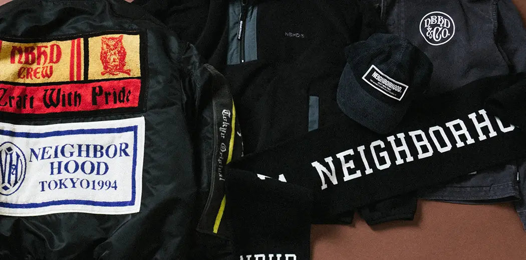 Black clothing set featuring a jacket with "Neighborhood & Co." patch, a cap with "Neighborhood" label, and a scarf with bold "NEIGHBORHOOD" text.