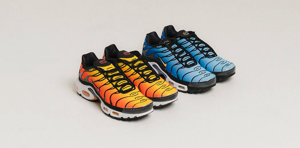 Two pairs of Nike Air Max Plus sneakers, one orange with yellow accents and the other blue, feature bold black swirl patterns on a neutral background.