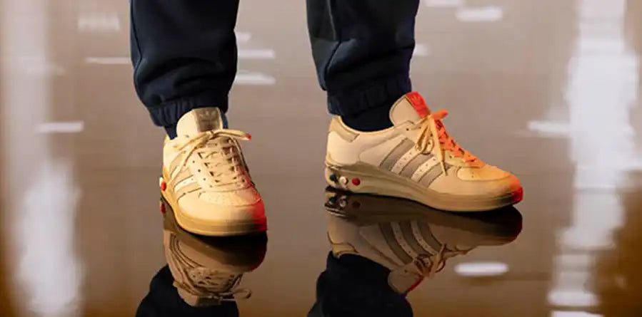 A pair of beige adidas SPZL sneakers with brown soles and signature stripes rests on a white modern chair. The setting is minimalistic and stylish.