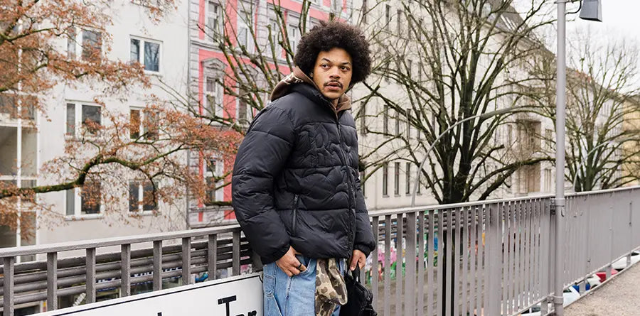 Model witn Puffer jacket leans on a rail, urban brackground
