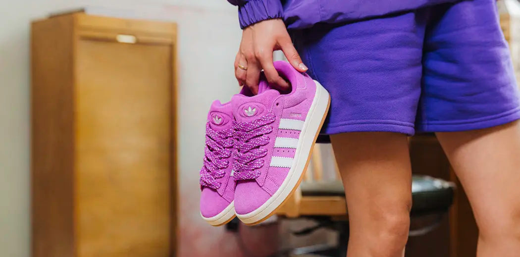 A woman tying her skateboarding sneakers on a wooden floor.
