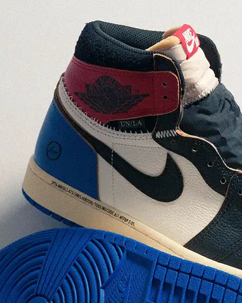 Close-up of a multicolored high-top sneaker Air Jordan 1 Fragm,ent x Union with red, white, and blue leather panels. It features black laces, a black swoosh, and a logo on the ankle. The sole is bright blue, giving a bold, stylish vibe.