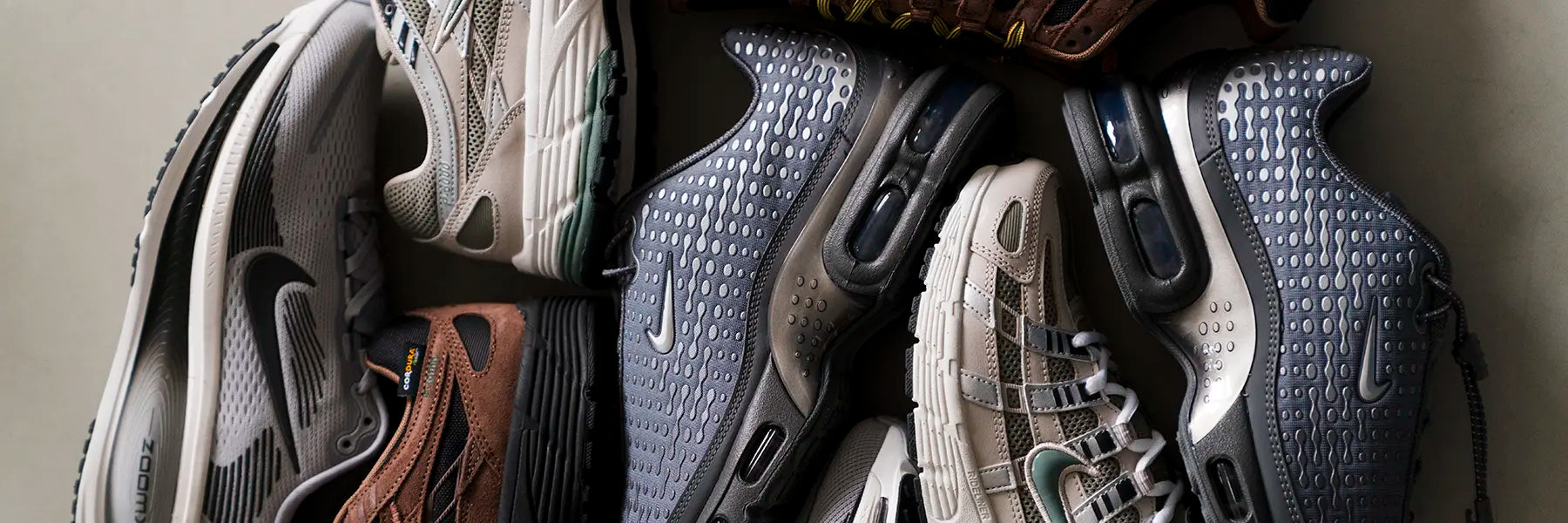 A collection of Nike sneakers in various neutral tones, arranged in a circular pattern on a light surface. The shoes feature diverse textures and designs.
