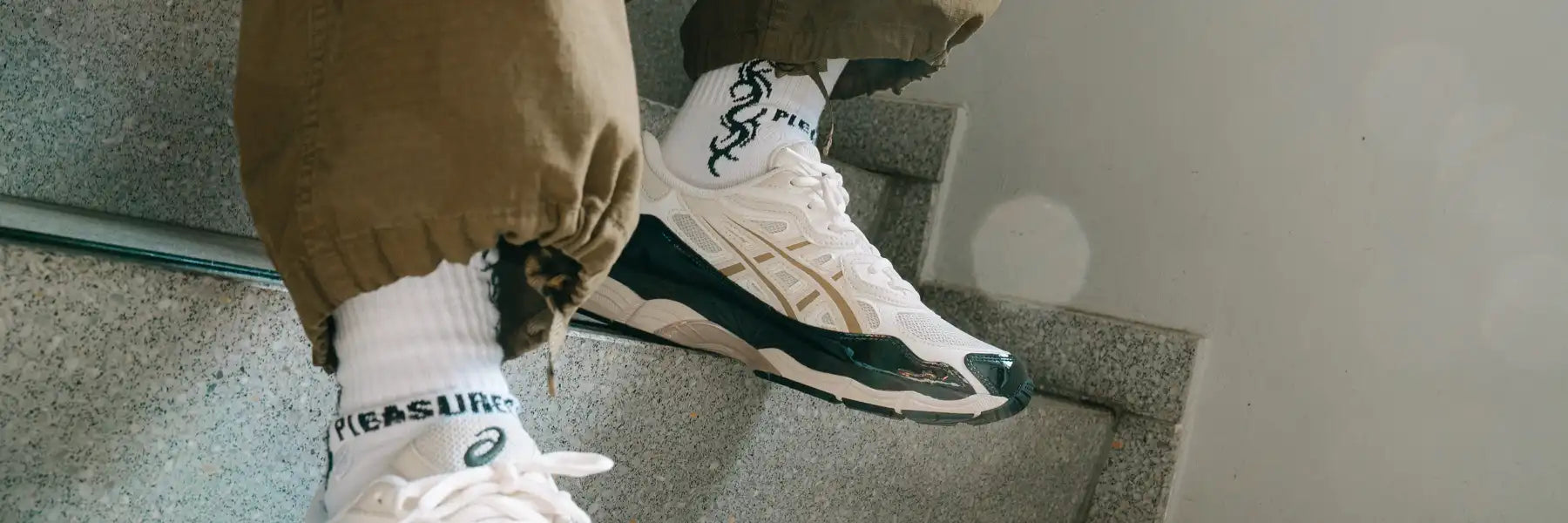 Person wearing white Asics sneakers with black and beige details and white socks with black tribal patterns sitting on stone stairs