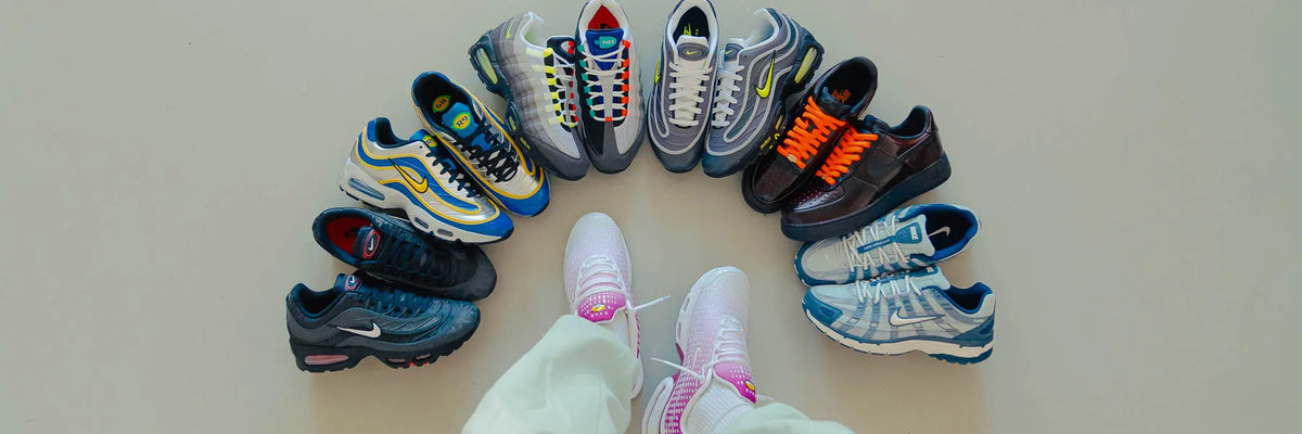Person wearing white sneakers standing in front of a semicircle of various Nike sneakers on a light floor