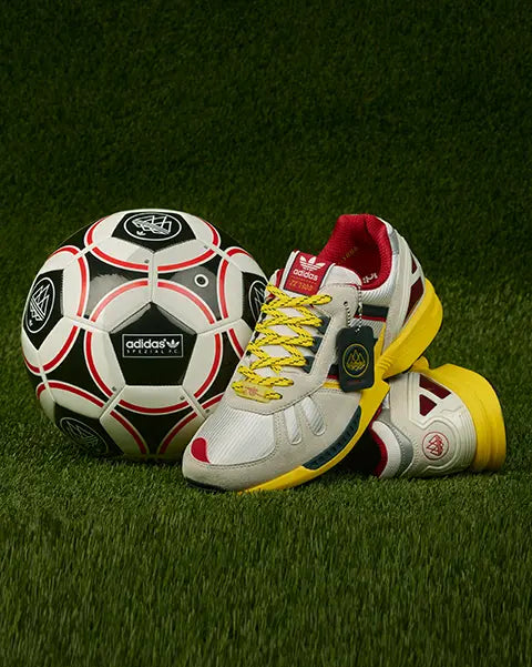 ZX Sneakers from the FC Arsenal x adidas SPZL F.C. drop discplayed on green grass next to a soccer ball from the same drop