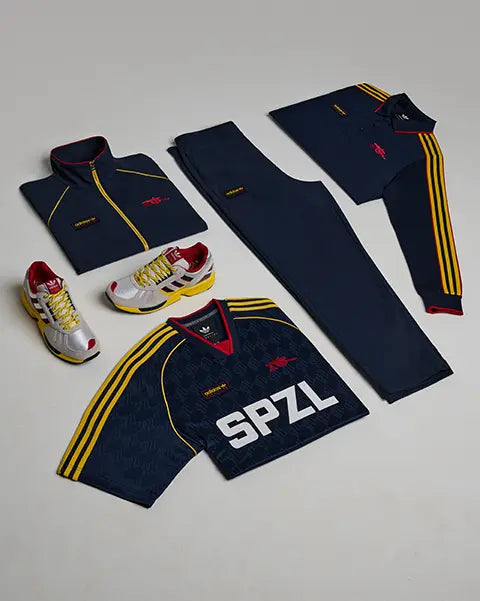 flatlay of Arsenal x adidas SPZL FC drop consisting of sneakers, jersey, longsleeve, track jacket and track pants in dark blue with yellow and red highlights