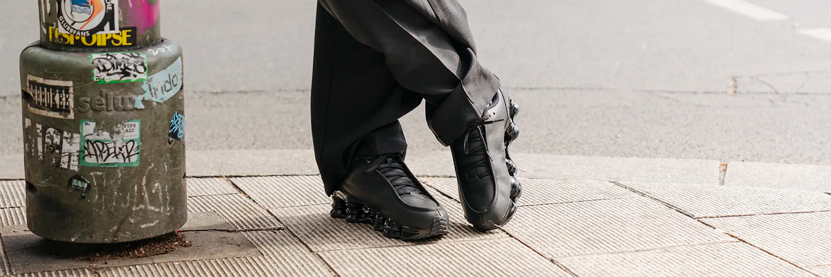 Person wearing black pants and black Nike Shox sneakers with segmented soles standing on tiled floor