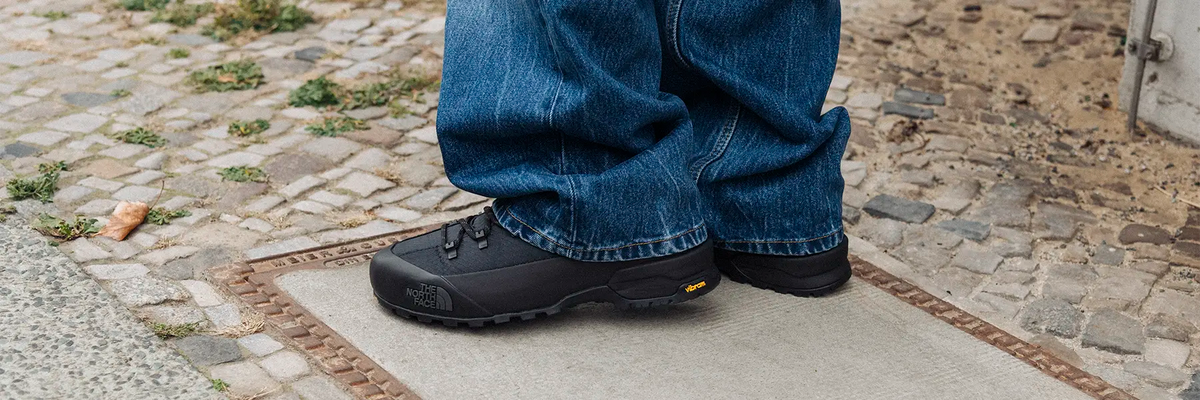Person wearing waterproof sneakers and blue jeans standing on a stone pavement
