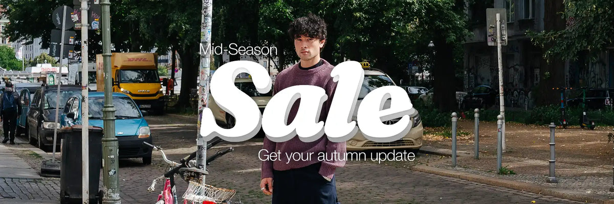 A man stands on a city street with trees, parked cars, and storefronts in the background. Large overlaid text reads 'Mid-Season Sale' and 'Get your autumn update'.