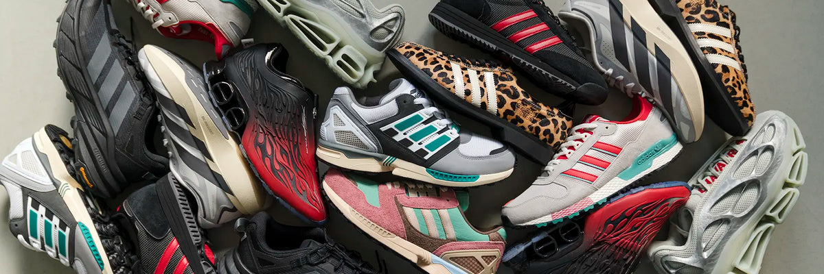 A dense, angled pile of various sneakers from Adidas, featuring multiple colorways including leopard print, red, teal, pink, black, and white.