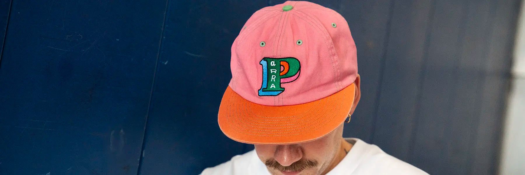 A person wearing a pink and orange cap with colorful embroidery. The cap features a stylized letter "P" and the word "Parra." The mood is casual.