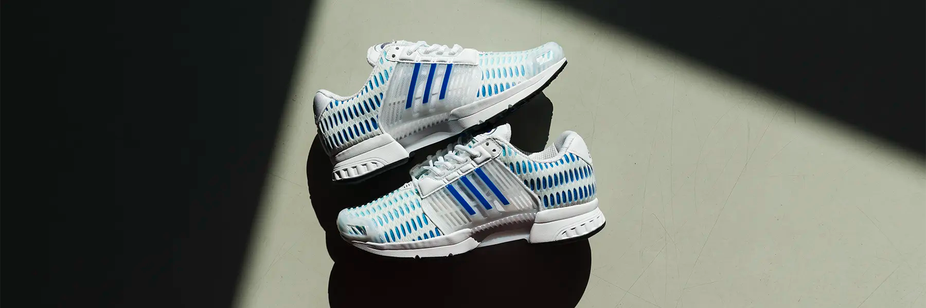 Pair of white adidas Climacool athletic shoes with blue stripes and ventilation holes on a dark surface