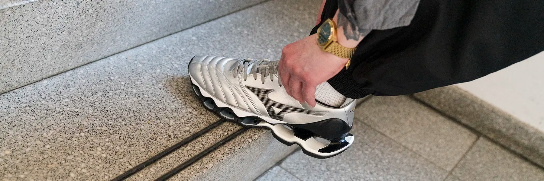 A person adjusts their silver athletic shoe on a textured stair. The scene conveys attention to detail and readiness, with a focus on the shoe's design.