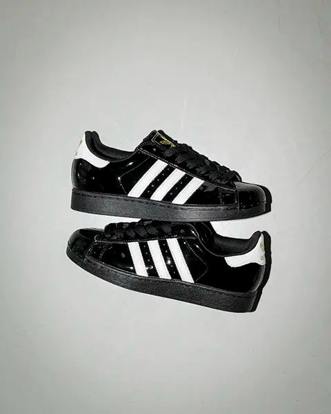a pair of black adidas superstar with white stripes made of shiny patent leather