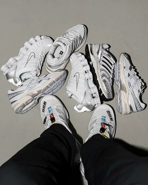 A person poses next to a variety of all white sneakers arranged in a casual setting.