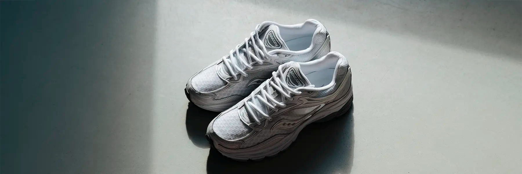 Pair of white Saucony running shoes with laces on a gray surface casting shadows