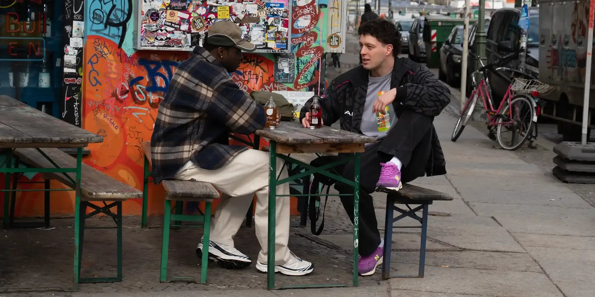 Two students sitting at a table in an urban setting with graffiti on the wall.